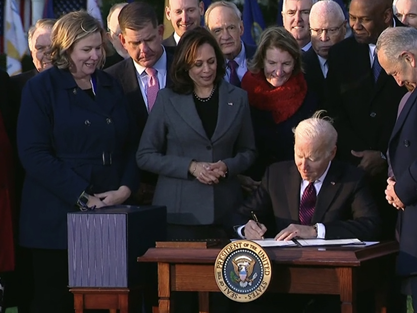 President Biden signs the bipartisan Infrastructure Investment and Jobs Act, surrounded by congressional leaders and supporters of the bill.